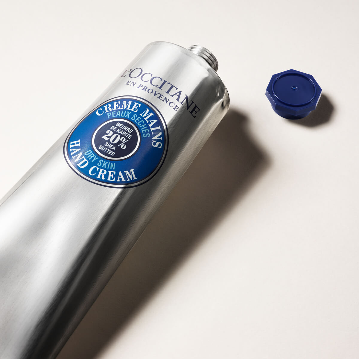 Krema za roke za suho kožo s karitejevim maslom L'Occitane - srebrna tuba in odprt pokrovček modre barve 
