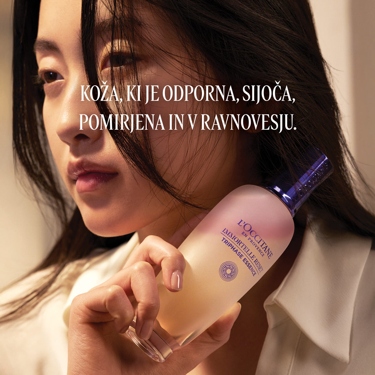 Ženska, ki ob obrazu drži izdelek L’Occitane Trifazna esenca za obraz - Immortale Reset kolekcija