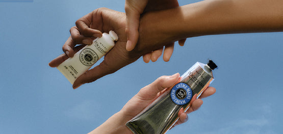 Iztegnjene roke držijo tube L'Occitanovih krem za roke