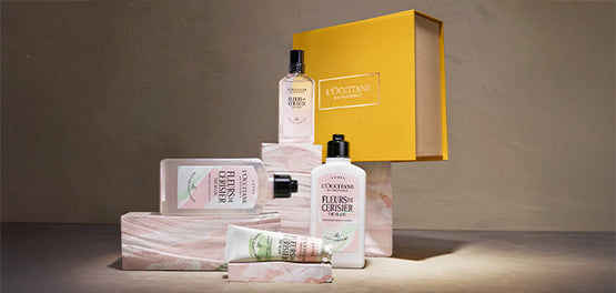 Kolekcija Fleurs de Cerisier Thé Blanc in darilna škatla v rumeni barvi, postavljeni na marmoriano glino v nežno roza barvi.  