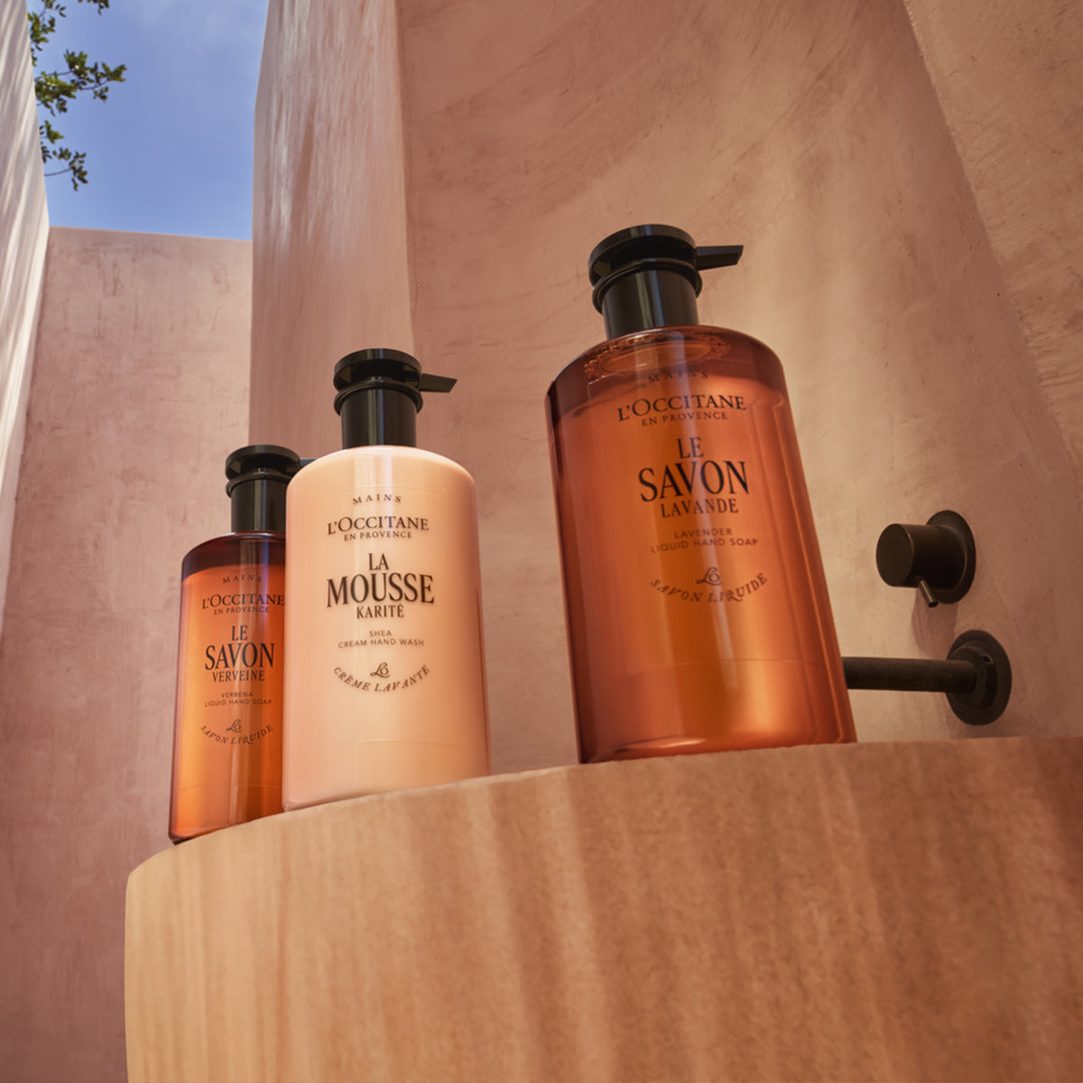 Tekoča mila Karite v elegantni stekleni embalaži, postavljena v zunanjo kopalnico v prefinjeni opečnati kopalnici 