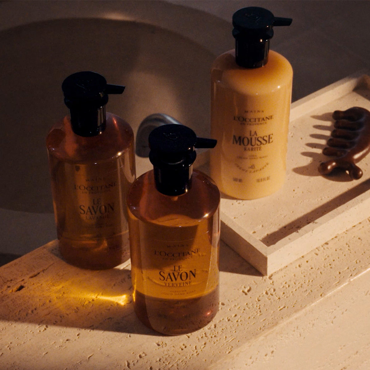 Tekoča mila Karite v elegantni stekleni embalaži, postavljena na prefinjeno kamnito podlago v kopalnici - L'Occitane 