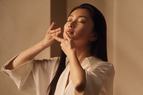 Ženska, ki kaže postopek masiranja obraza in nanašanja produkta - L'Occitane.