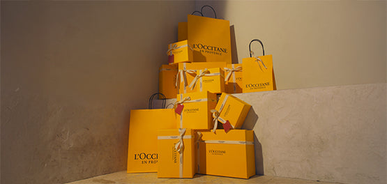 L’Occitanove darilne škatle in darilne vrečke v rumeni barvi, zložene ena na drugo 