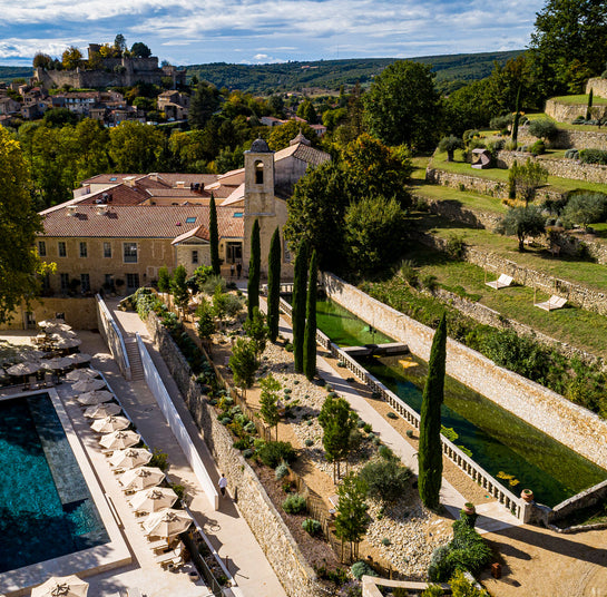 Okolica provansalske hiše z bazenom, terasami in zelenjem. V ozadju se vidi vas na hribu. - L'Occitane