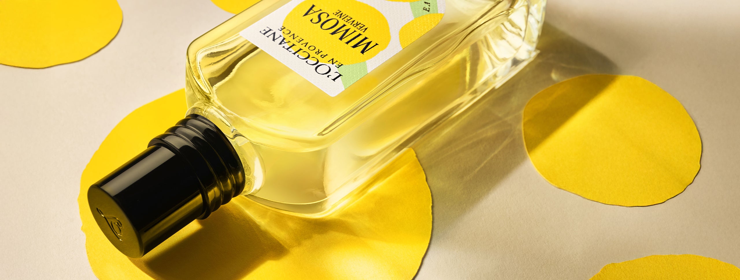 Eau de Toilette iz dišavne kolekcije Mimosa Verveine na podlagi z rumenimi krogi, ki uprizarjajo provansalsko zimsko sonce - L'Occitane.