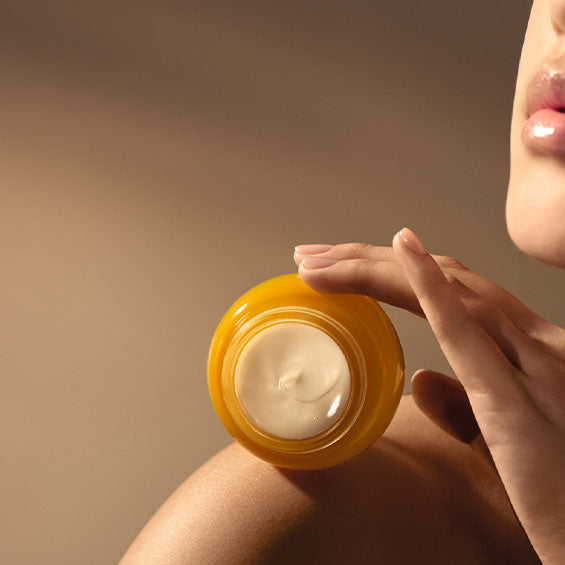 Odprta L'Occitane Božanska krema za obraz v rumeni steklenički na goli ženski rami  