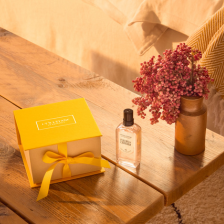 Rumen darilna škatla L'Occitane na mizi poleg dišave in rože.