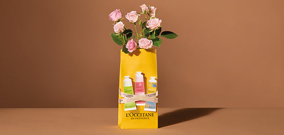 Roza vrtnice in tri kreme za roke L’Occitane na rumeni darilni vrečki L’Occitane 