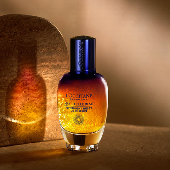 Steklenička Boosterja za nočno nego obraza Immortelle Reset in njen odsev – L’Occitane 