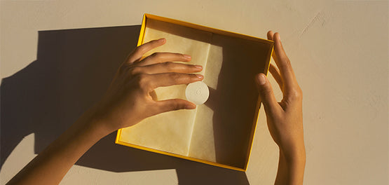 Ženske roke, ki z nalepko L’Occitane lepijo zapirajo okrasni darilni papir v L’Occitane darilni škatli 