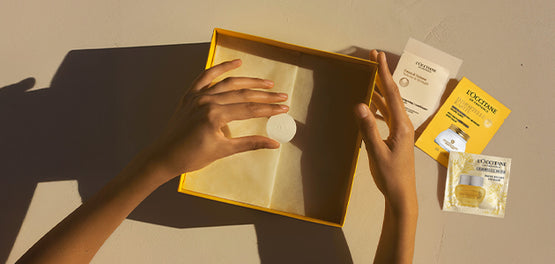 Ženske roke, ki z nalepko zapirajo okrasni darilni papir, lično zložen v darilno škatlo L’Occitane 