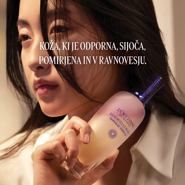 Ženska, ki ob obrazu drži izdelek L’Occitane Trifazna esenca za obraz - Immortale Reset kolekcija