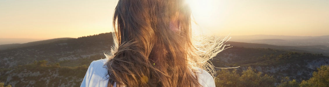 Ženska z dolgimi, lepimi lasmi gleda proti sončnemu zahodu 